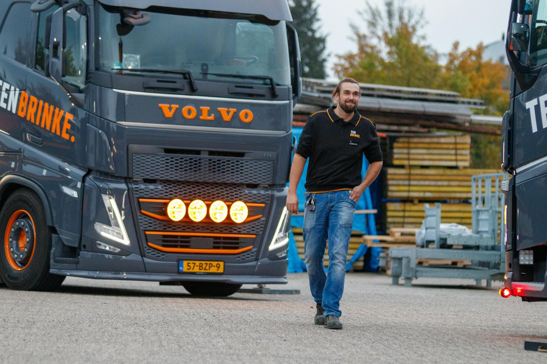 Truck driver walking near a Volvo truck in an industrial area during the day, showcasing logistics and transportation.