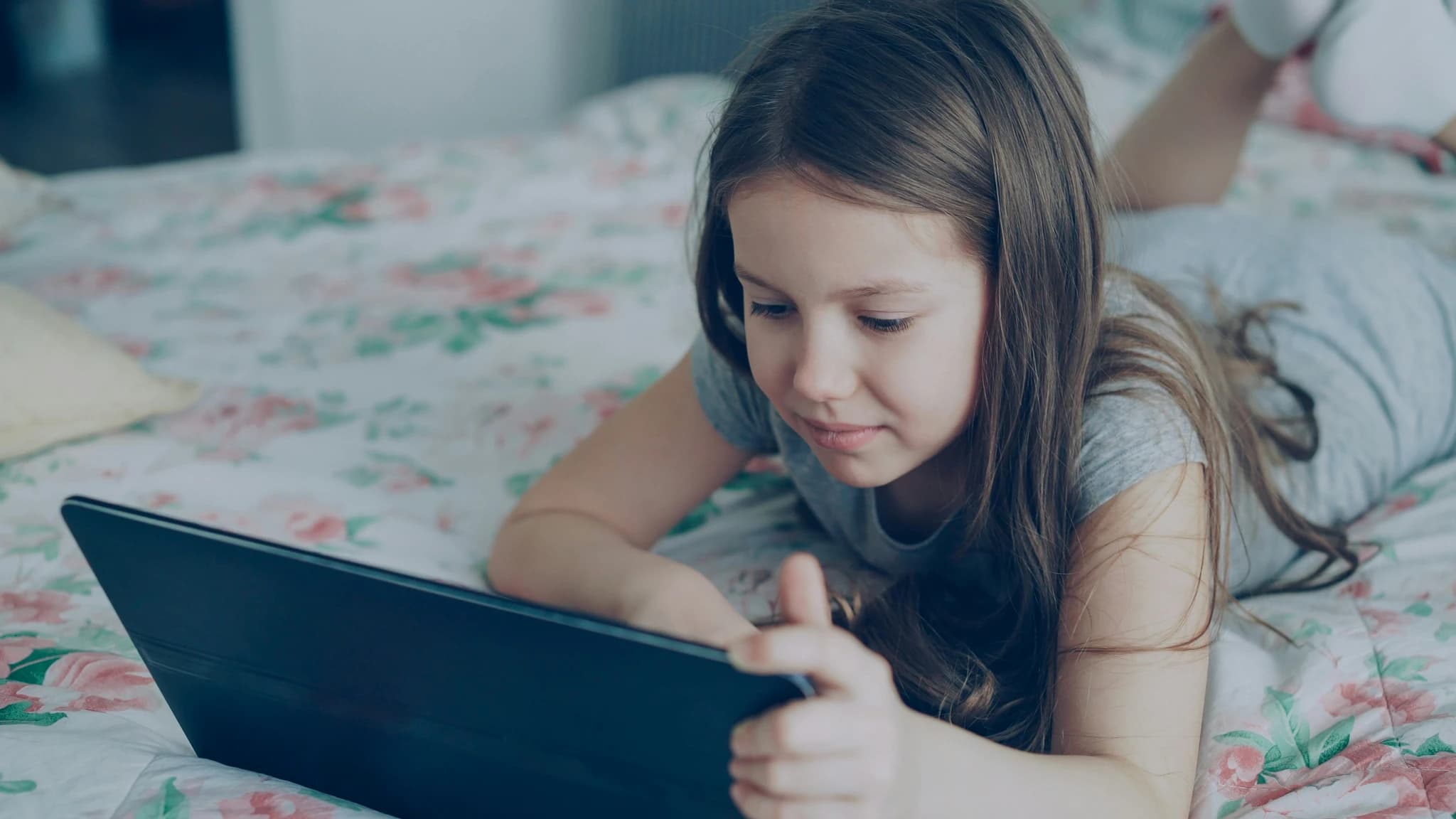 A girl is using a tablet on her bed.