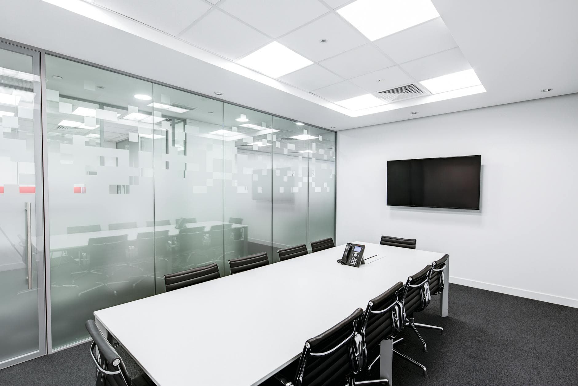 Sleek, minimalist conference room with glass walls, long table, and office chairs.