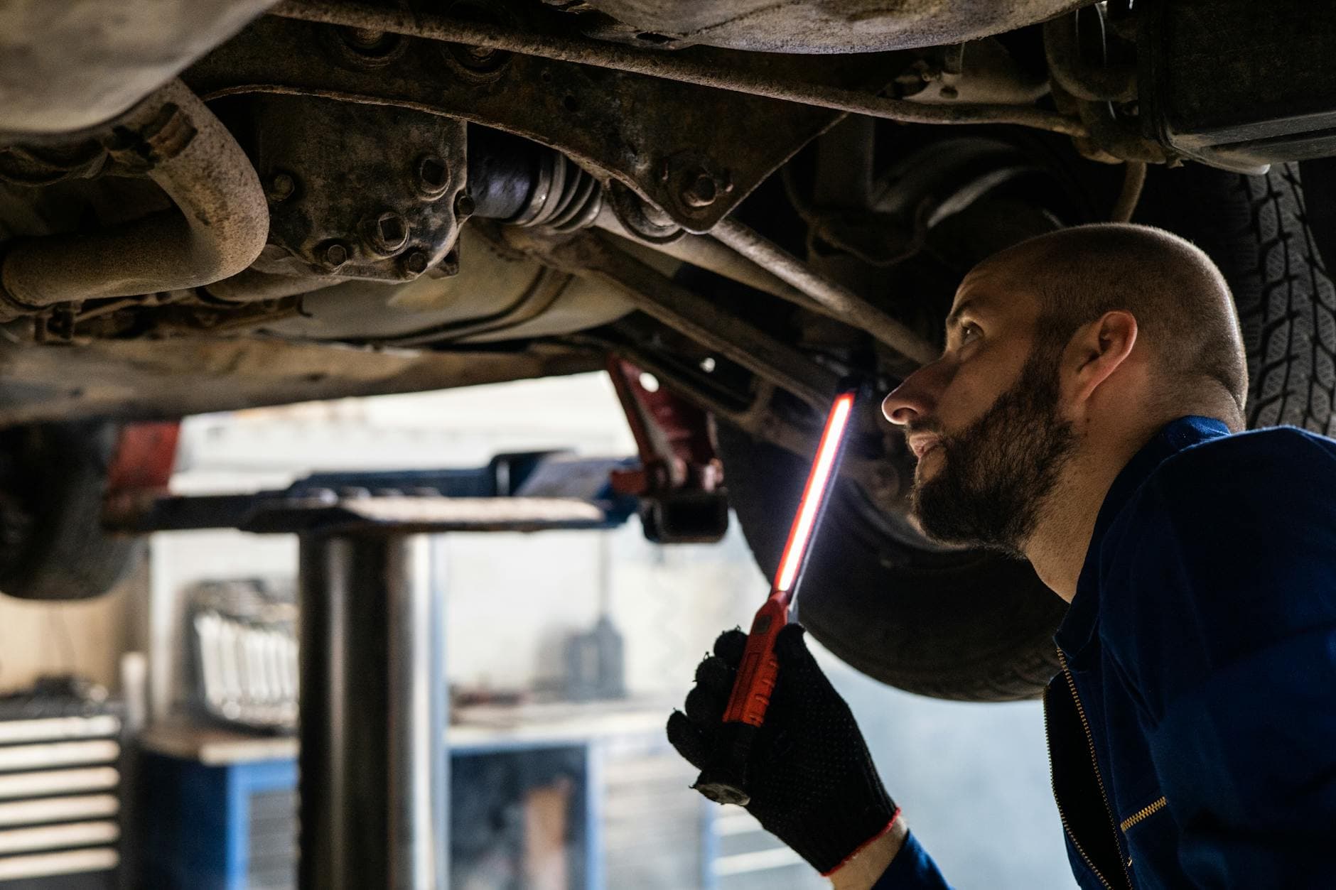 Mechanic using light to inspect vehicle undercarriage in workshop for maintenance.