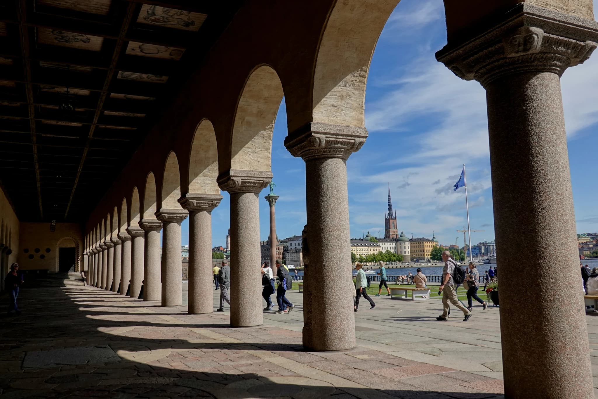 a group of people walking down a sidewalk next to tall pillars