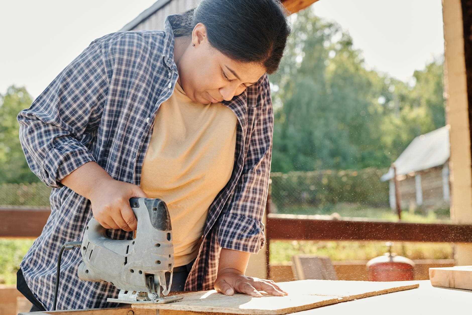 Focused woman using a jigsaw to cut wood outdoors. Ideal for carpentry, construction themes.