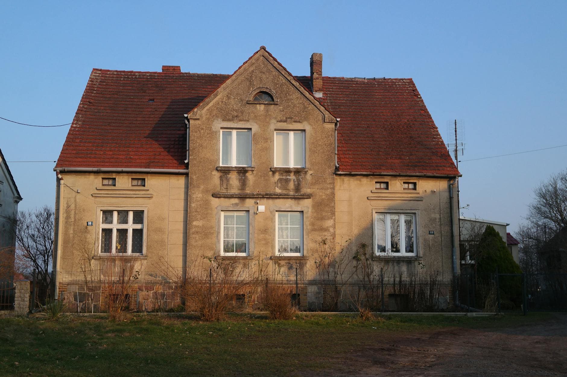 Old European-style house with red roof and beige walls in sunlight.