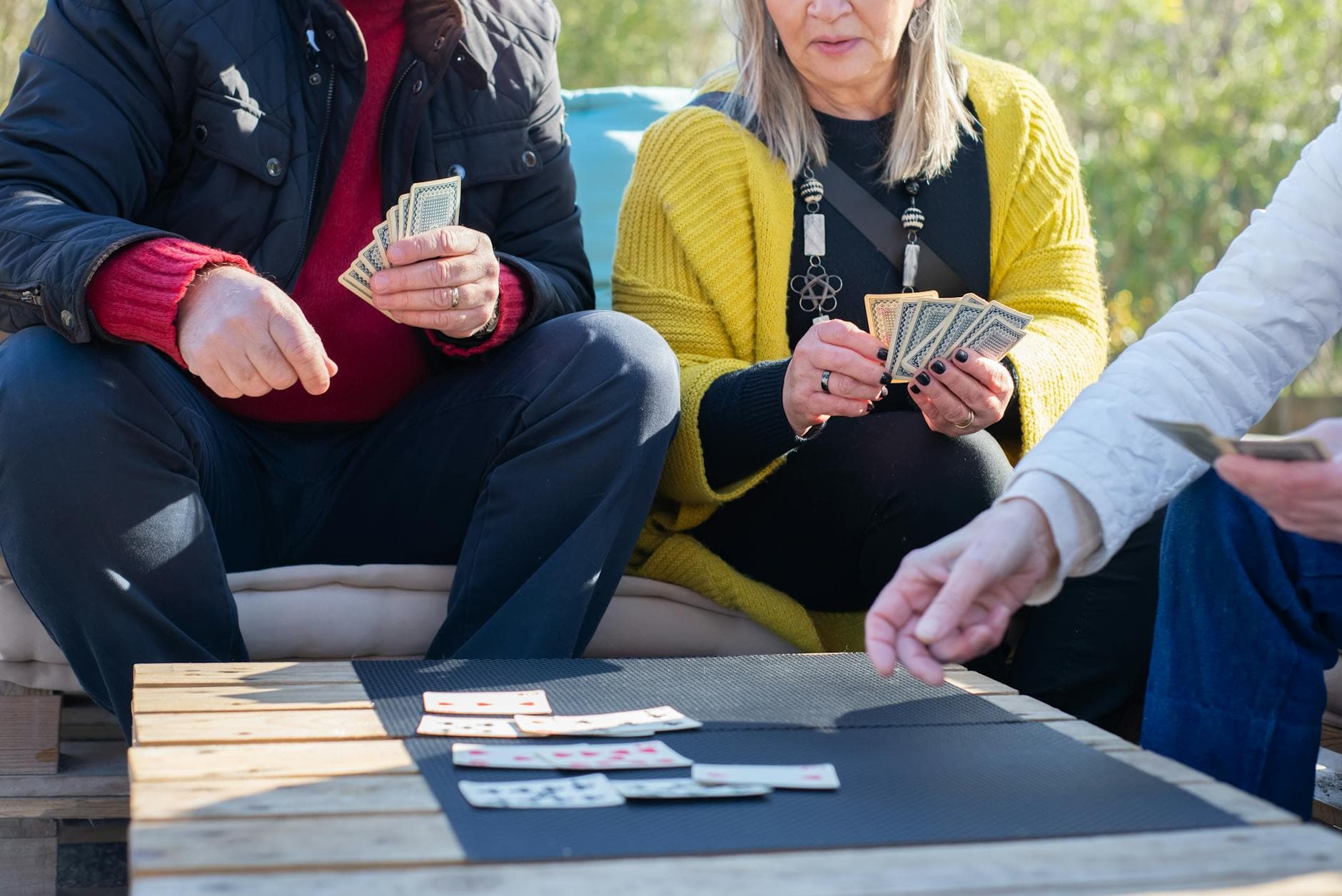 Seniors playing cards at an outdoor table, enjoying leisure time together under the sun.
