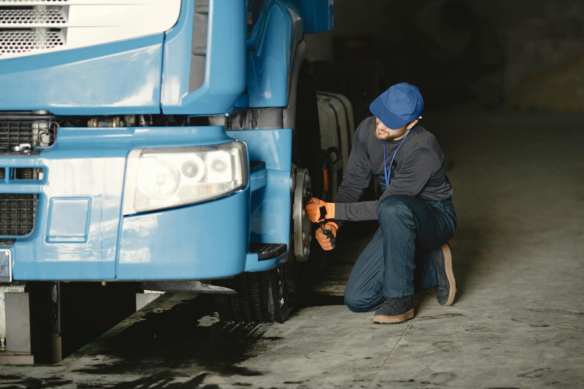 Mechanic in a garage fixing the wheel of a blue truck. Industrial vehicle maintenance.